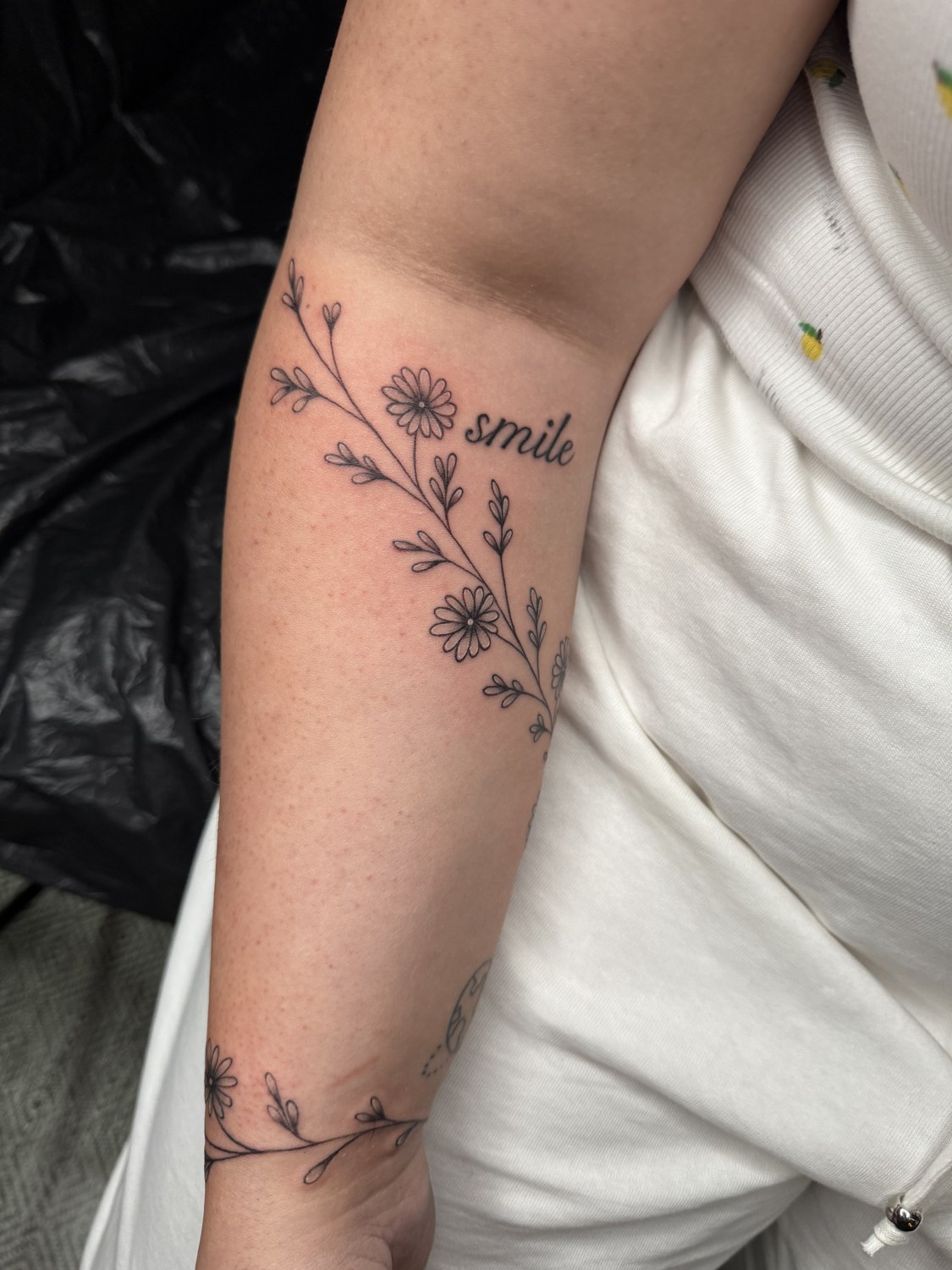 Feine Blumenranke mit Gänseblümchen und smile-Lettering am Arm