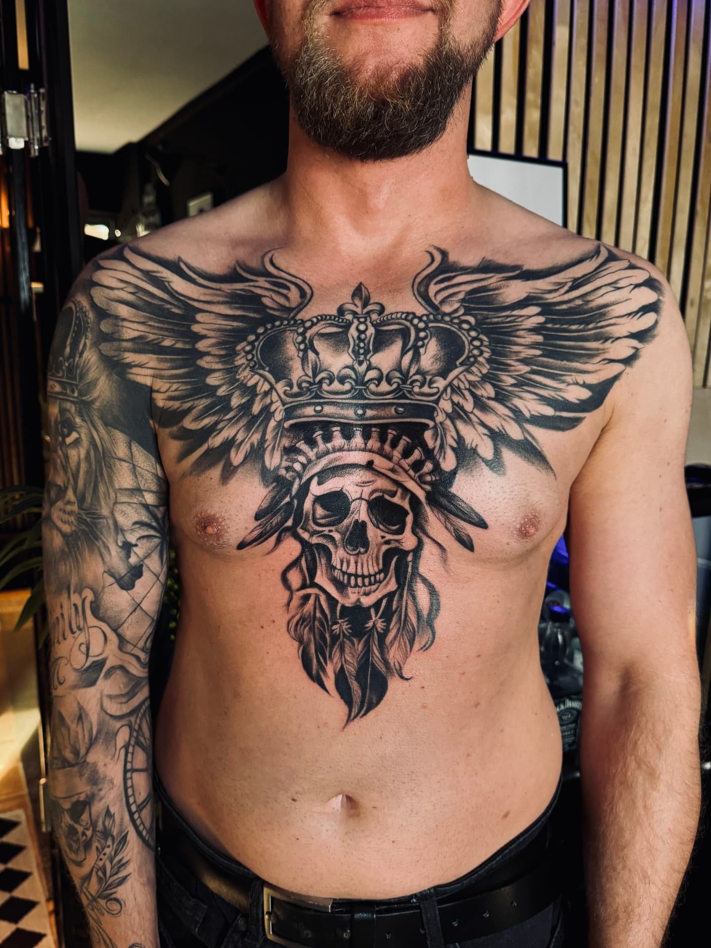 Brust-Tattoo mit gekröntem Totenkopf, Flügeln und Federn