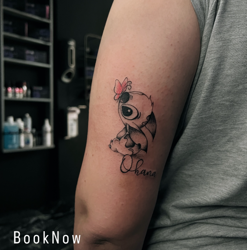 Stitch Tattoo mit Schriftzug Ohana und rotem Akzent am Oberarm
