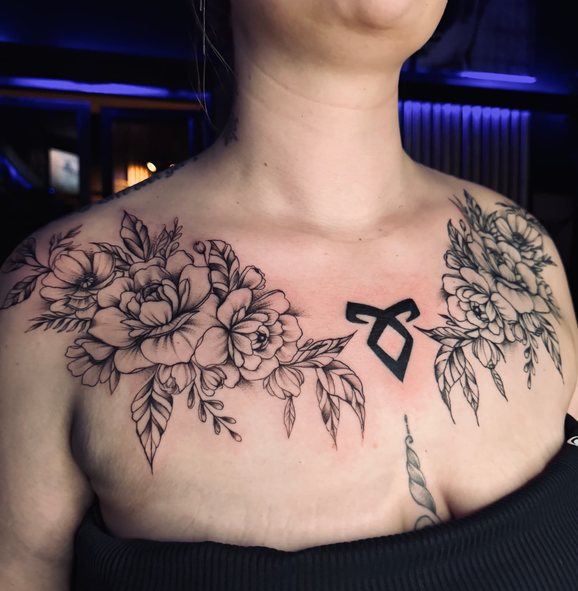 Fineline Blüten über Schlüsselbein und Brust mit Rune