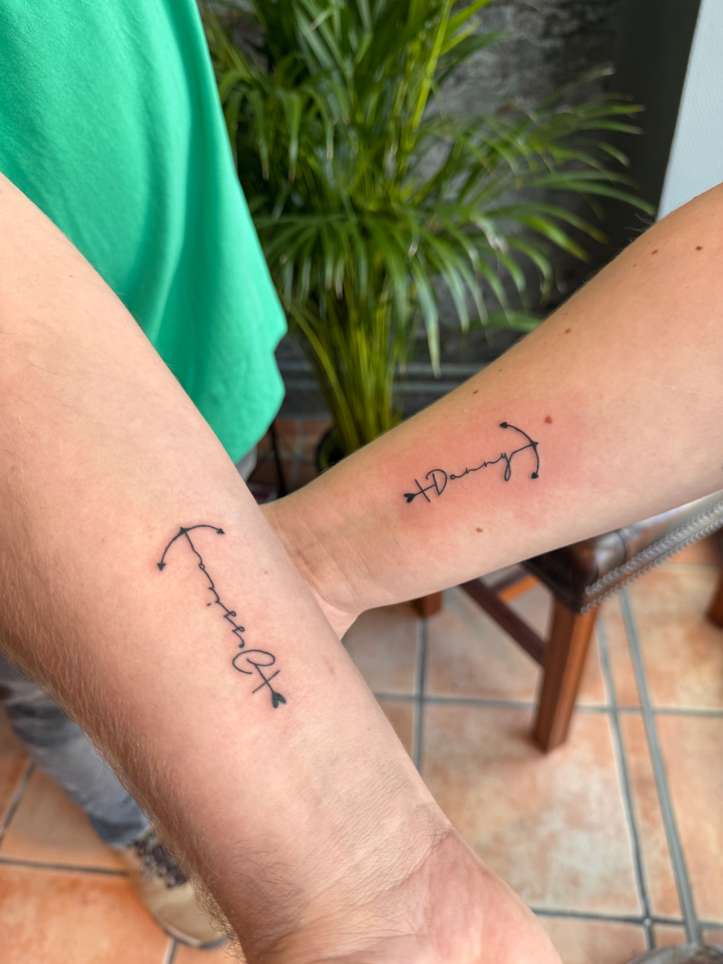 Partner-Tattoos mit Namen Danny und Pfeil-Schriftzug am Unterarm in Fineline