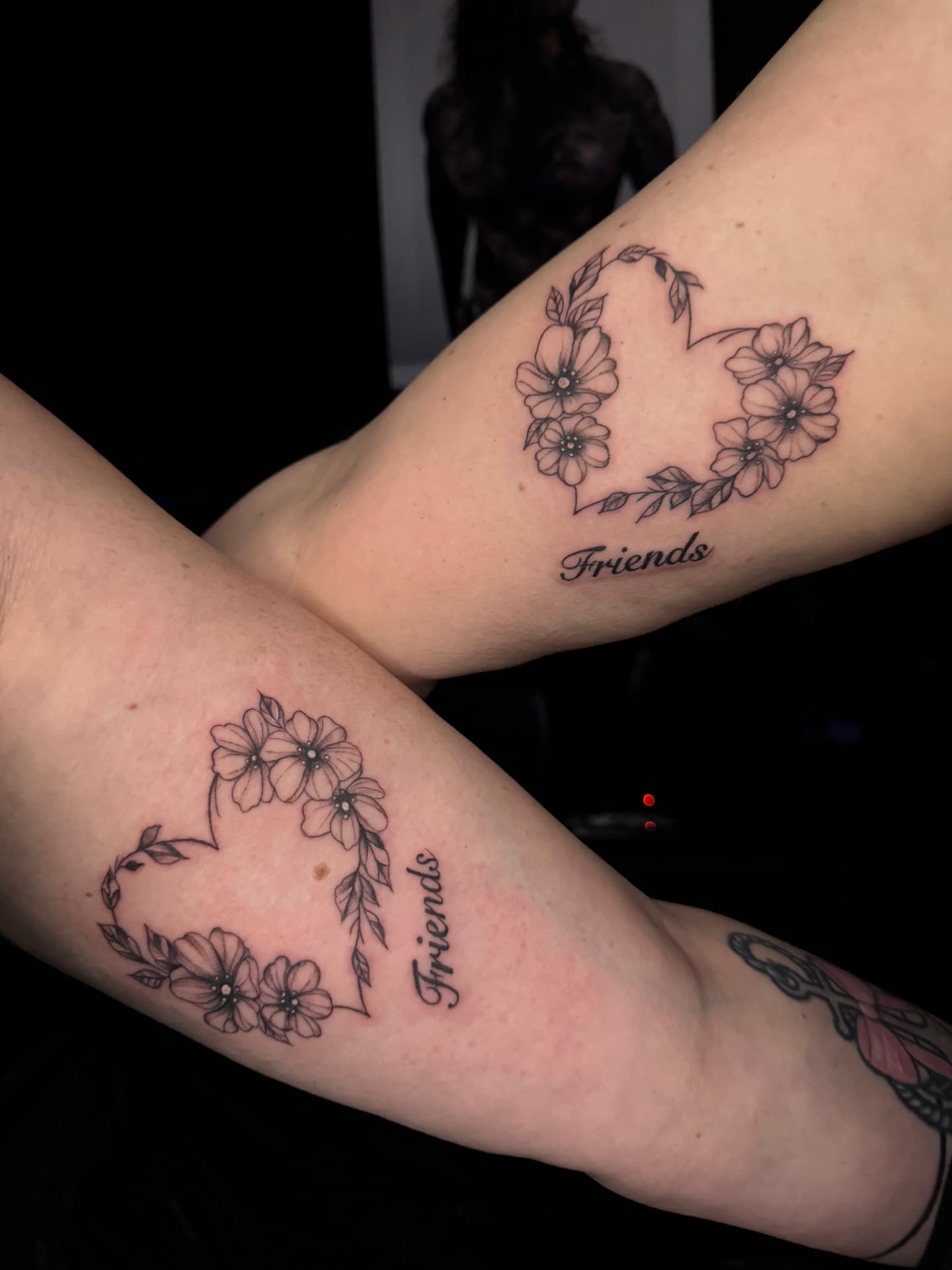 Partner-Tattoos mit Blumenherz und Friends-Lettering am Oberarm